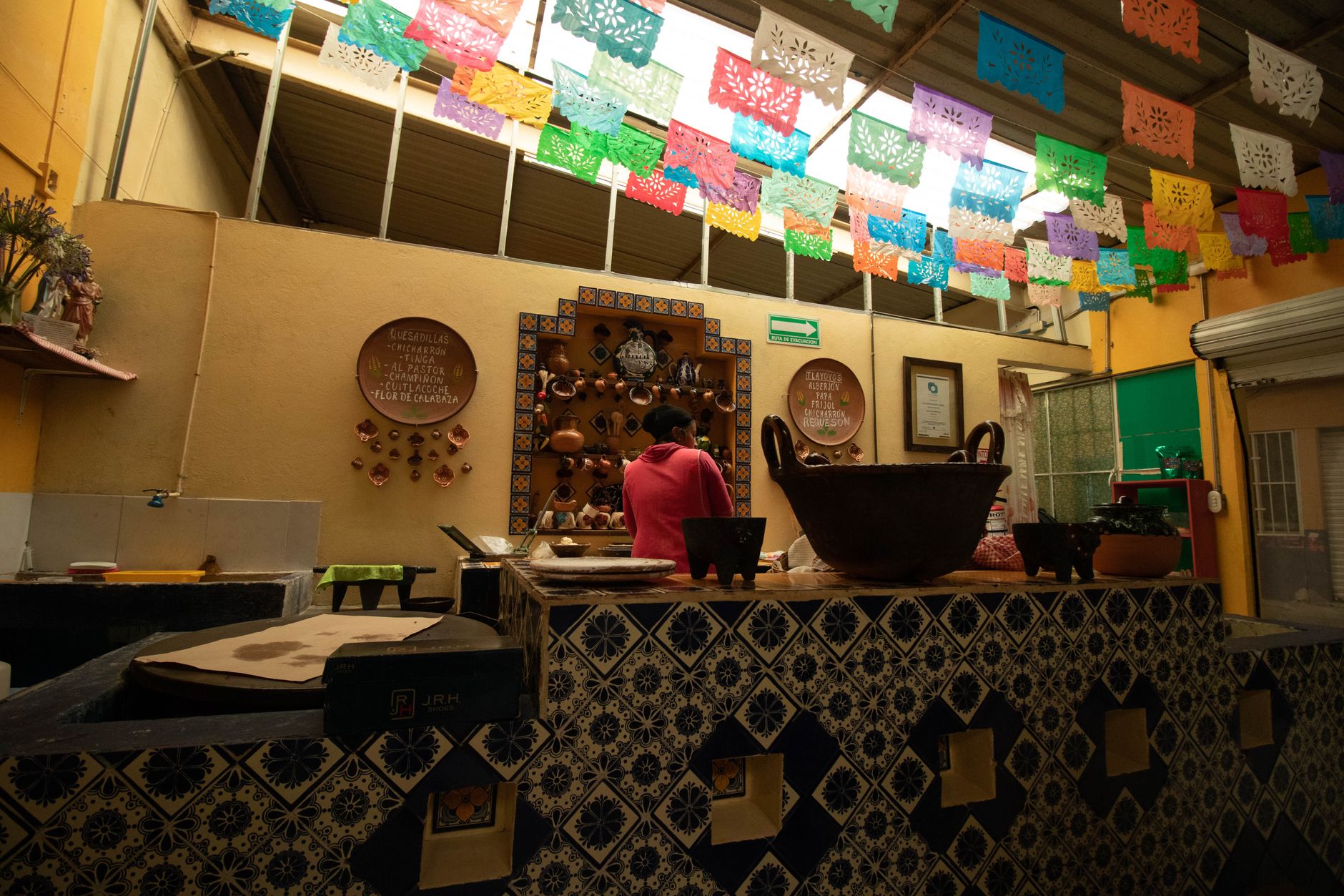 Inside Taqueria Hernandez's kitchen counter, hand-painted Talavera tile, papel picado banners overhead, and a handwritten menu board.