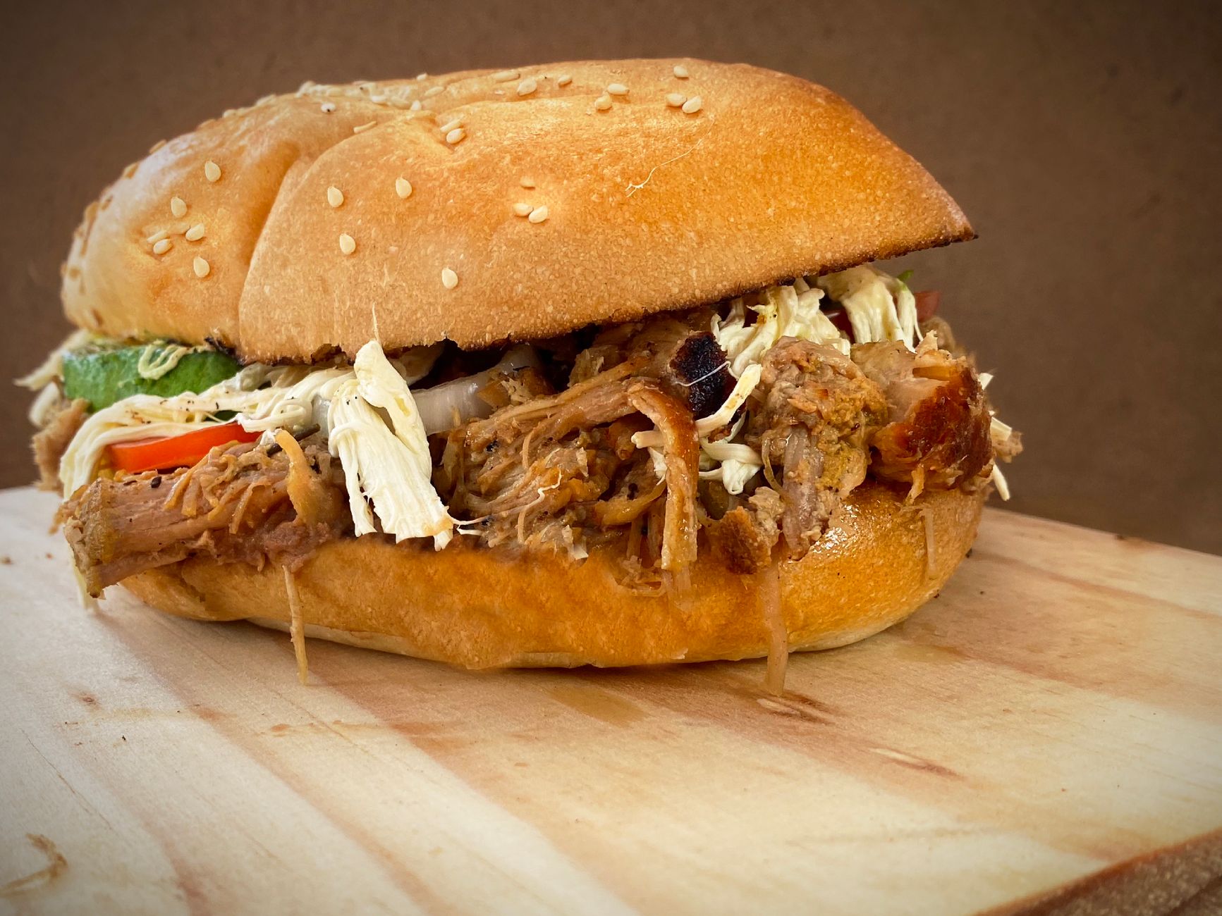 A Mexican torta sandwich stacked with pulled meat, avocado, tomato and onion on a sesame roll.